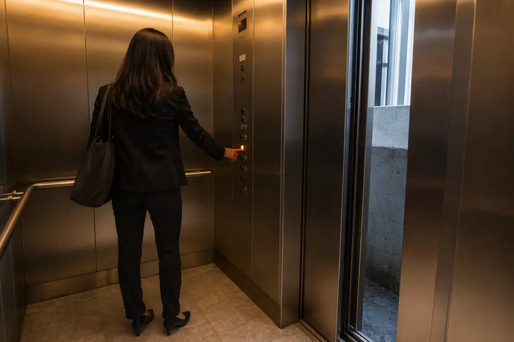 Passenger pressing the emergency call button inside a stalled elevator cab during an entrapment, with the door gap visible above the landing level in a Washington DC office building.