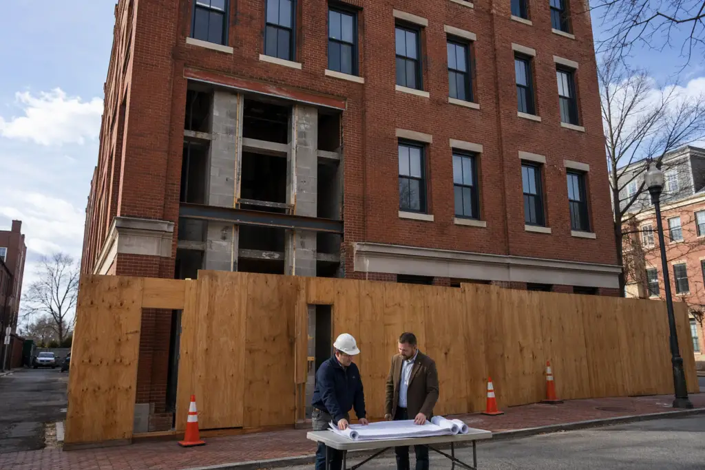 Structural engineer and building owner reviewing retrofit elevator installation plans outside a 4-story brick commercial building in Baltimore, MD