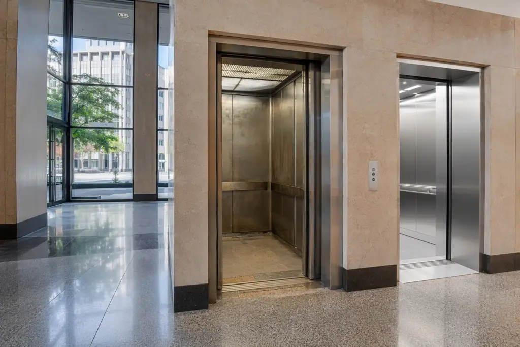 Two commercial elevator cabs side by side in a Washington DC office lobby — one aged and worn, one modernized — illustrating commercial elevator lifespan and repair vs. replacement decisions.