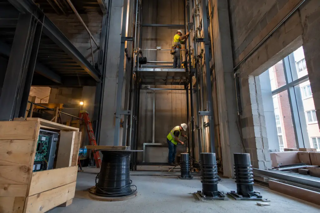 Licensed elevator mechanics installing guide rails inside a steel-framed hoistway during new elevator construction in a Baltimore MD commercial building